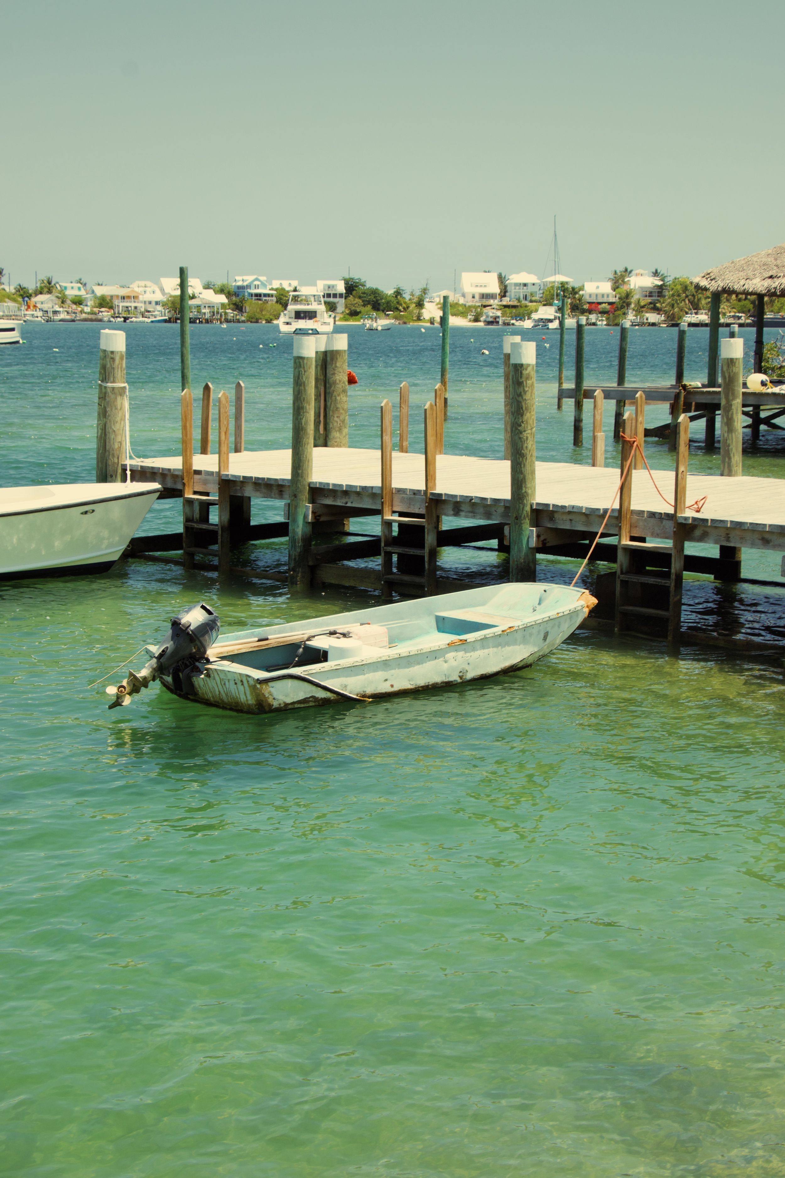 Small motorboat docked at wooden pier in turquoise harbor waters.