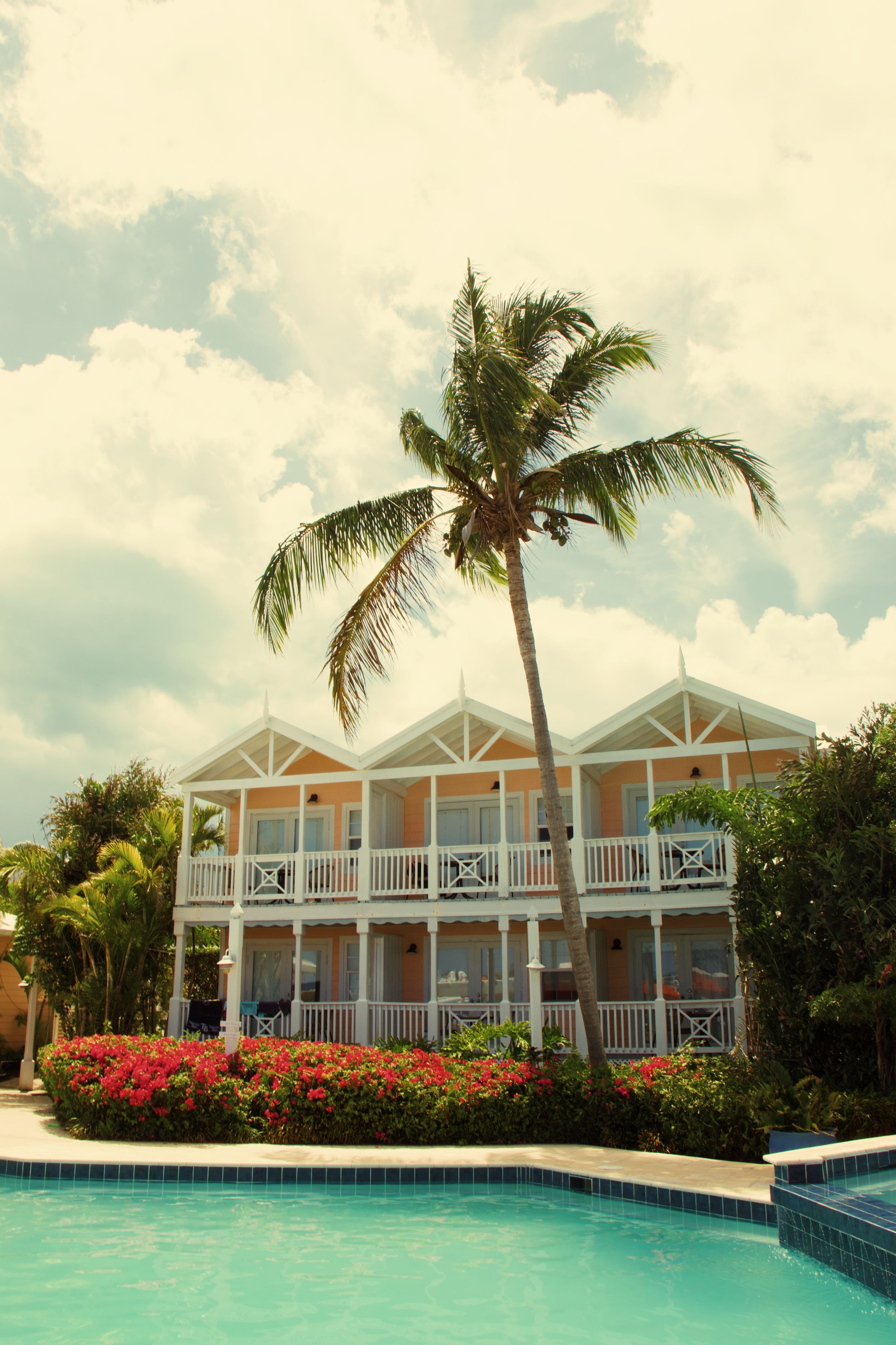 Tropical resort with two-story building and swimming pool surrounded by palm trees and bougainvillea.