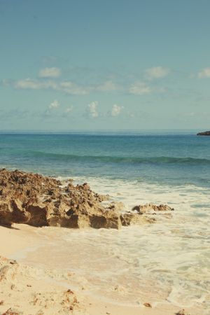 Rocky coastal beach with crashing waves against a turquoise ocean backdrop.
