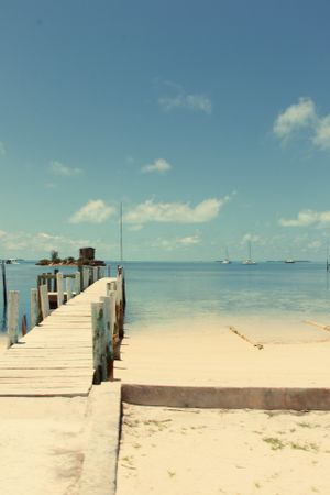 Wooden pier extends into tranquil turquoise waters under blue sky with white clouds.