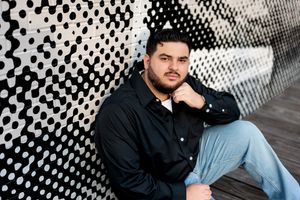 Young man in black shirt sitting against bold black and white geometric patterned wall.