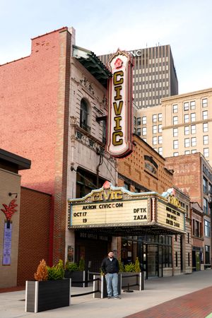 Male senior portrait subject standing before iconic Akron Civic Theatre marquee downtown.