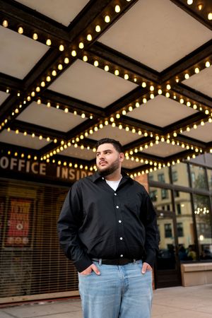 Young man in black shirt posing under glowing theater marquee lights at night.