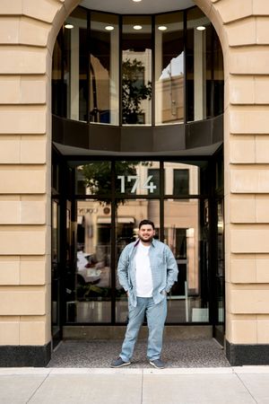 Smiling young man standing before elegant arched building entrance numbered 174.