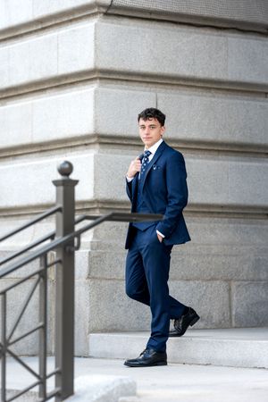 Stylish young man in navy three-piece suit posing on steps of stone building.