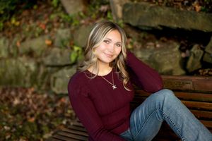 Smiling young woman in burgundy sweater sitting on a wooden bench in an autumn park setting.