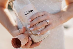Woman holding a personalized sand-filled bottle labeled Haley, wearing white nail polish and rings.
