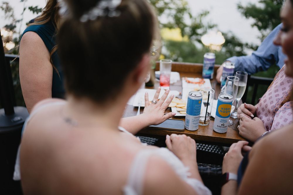 Bride sits at outdoor table with guests, drinks and snacks visible during wedding reception celebration.