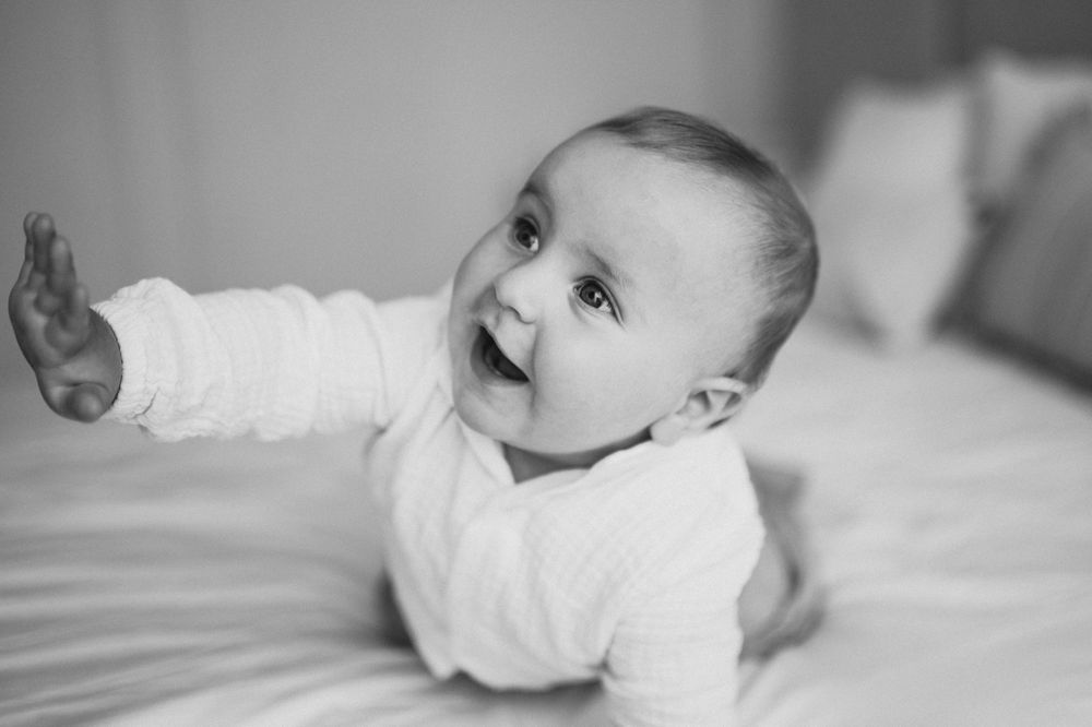 Adorable smiling baby lying on a bed reaching out with one arm in a black and white photo.