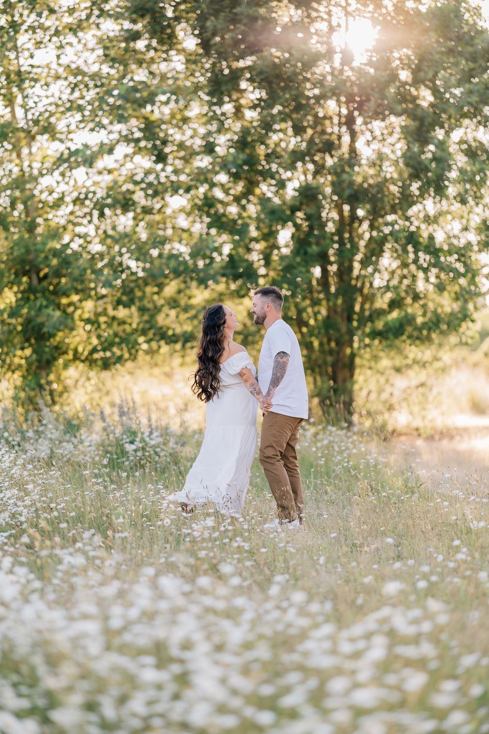 A couple holds hands and shares a romantic moment in a sunlit wildflower meadow.