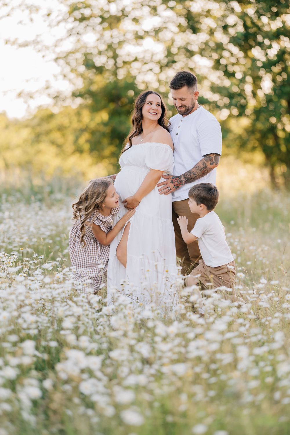 Happy pregnant woman in white dress with husband and two children in a sunny wildflower field.