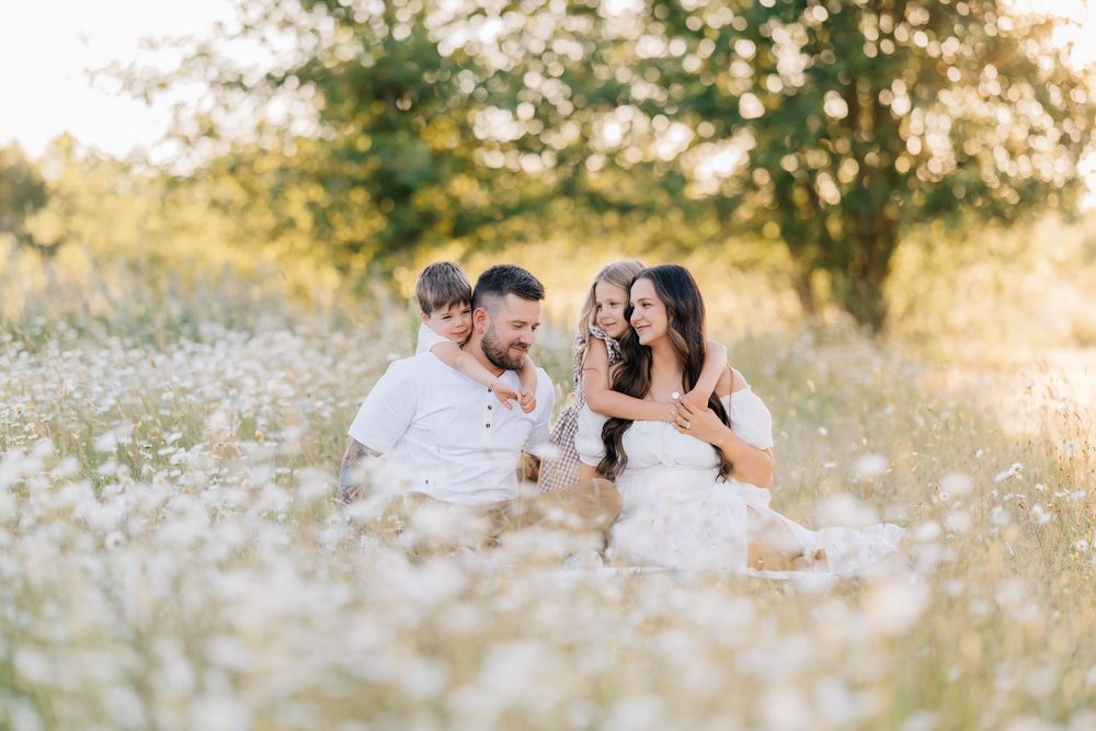 Happy family with two children sits together in sunlit daisy field for a warm outdoor portrait session.