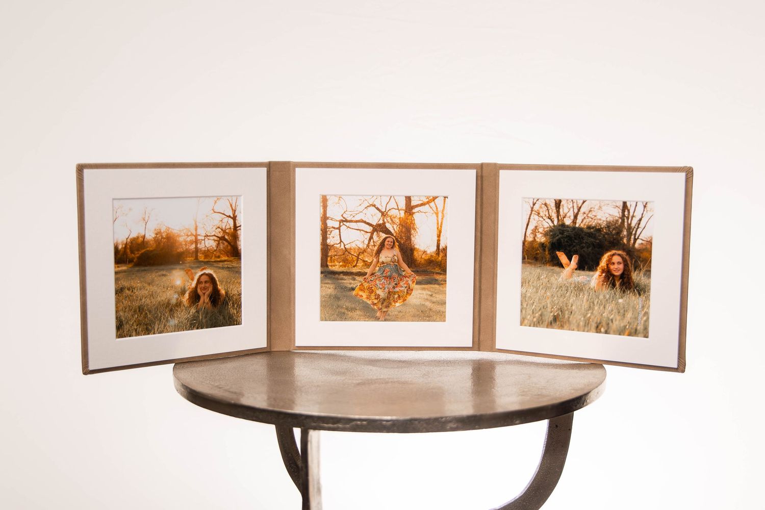 Triptych of framed photos of a woman in nature displayed on a round metal table against a white wall.