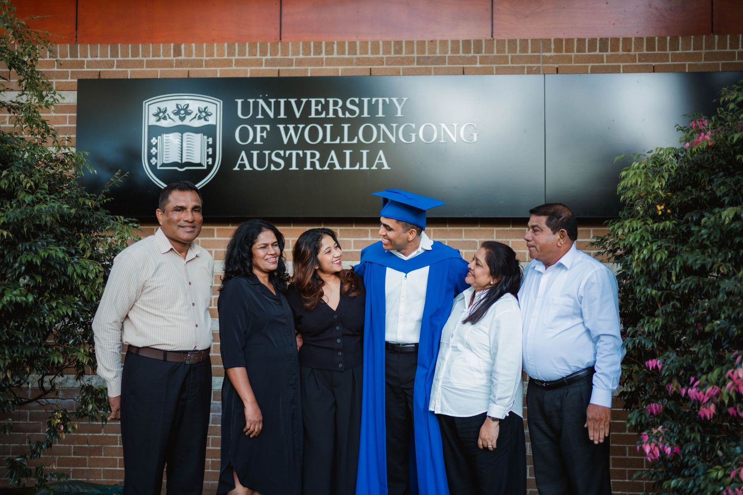 Graduate in a blue gown and cap poses with five family members in front of the University of Wollongong Australia sign.
