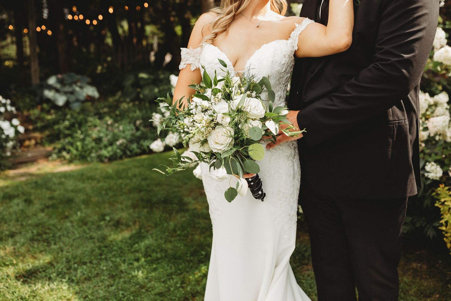 Close-up wedding portrait of a bride holding a white and green bouquet beside her groom in a black suit.