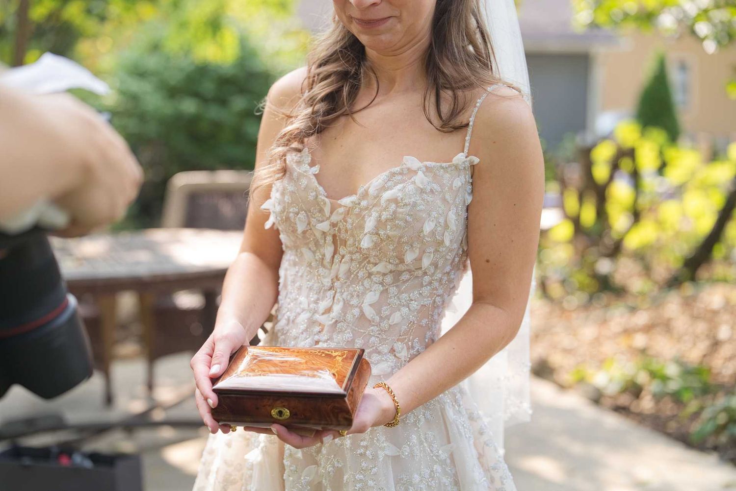 Bride in lace wedding gown holding a wooden ring box outdoors on her wedding day.