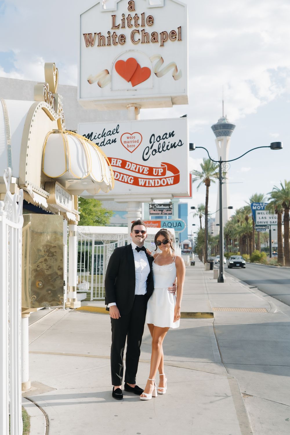 Couple poses in front of A Little White Chapel wedding venue on the Las Vegas Strip, bride in white mini dress.