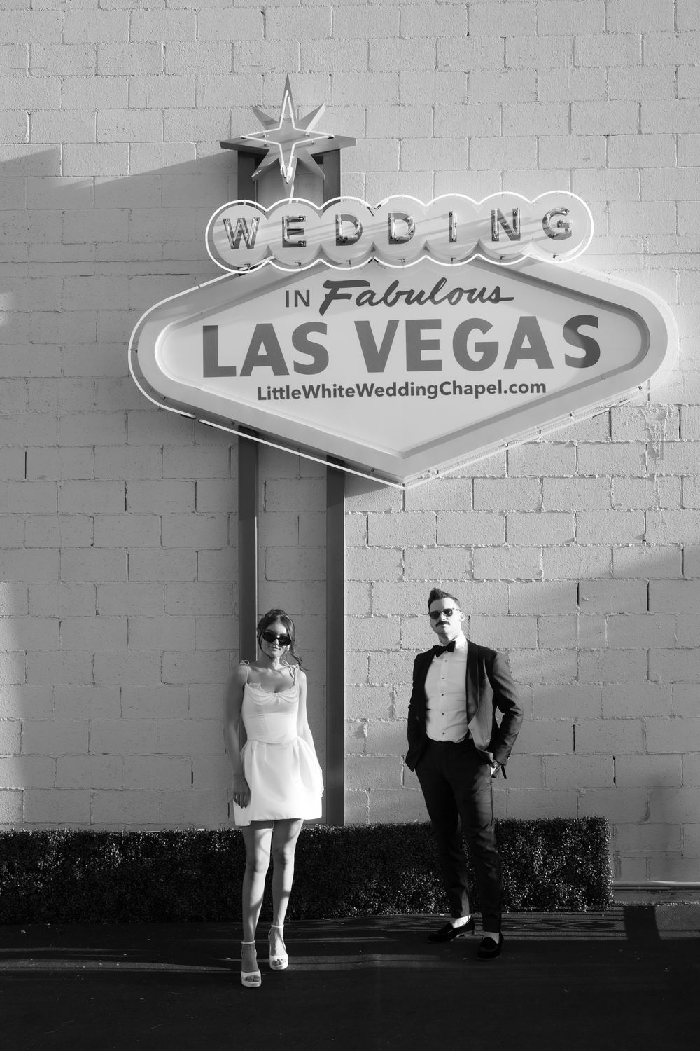 Couple posing under Wedding in Fabulous Las Vegas Little White Wedding Chapel sign in black and white photo.