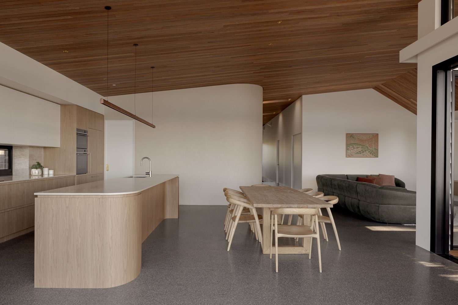 Open plan kitchen, dining and living area with a timber ceiling and warm oak joinery, interior photography on the NSW South Coast.