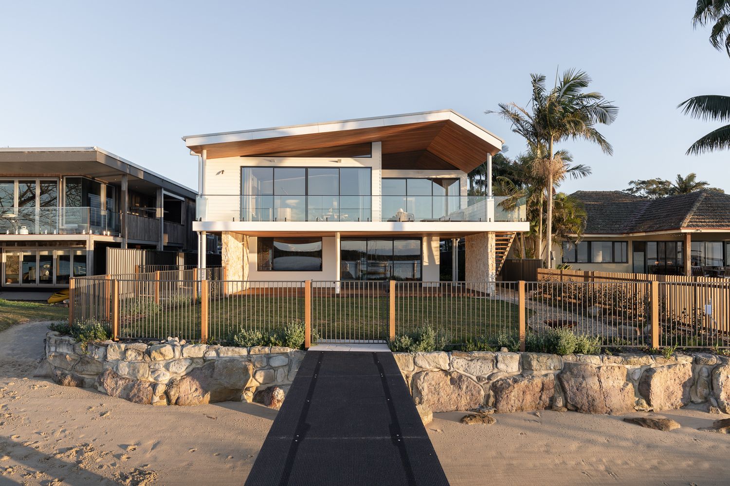 Riverfront new home in Shoalhaven NSW designed by iarchitecture, with a raked timber roofline and a path leading up from the river.