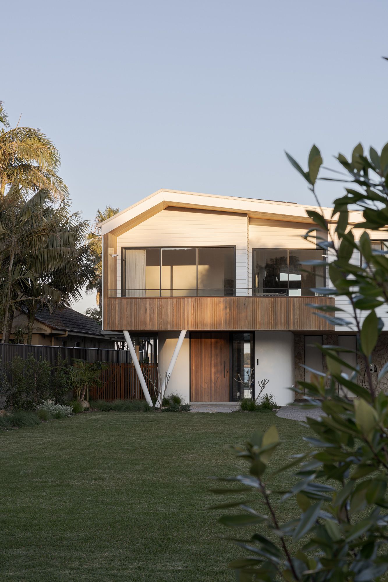 Front facade of a new, residential home in Shoalhaven NSW with timber cladding, angled white columns and native garden.