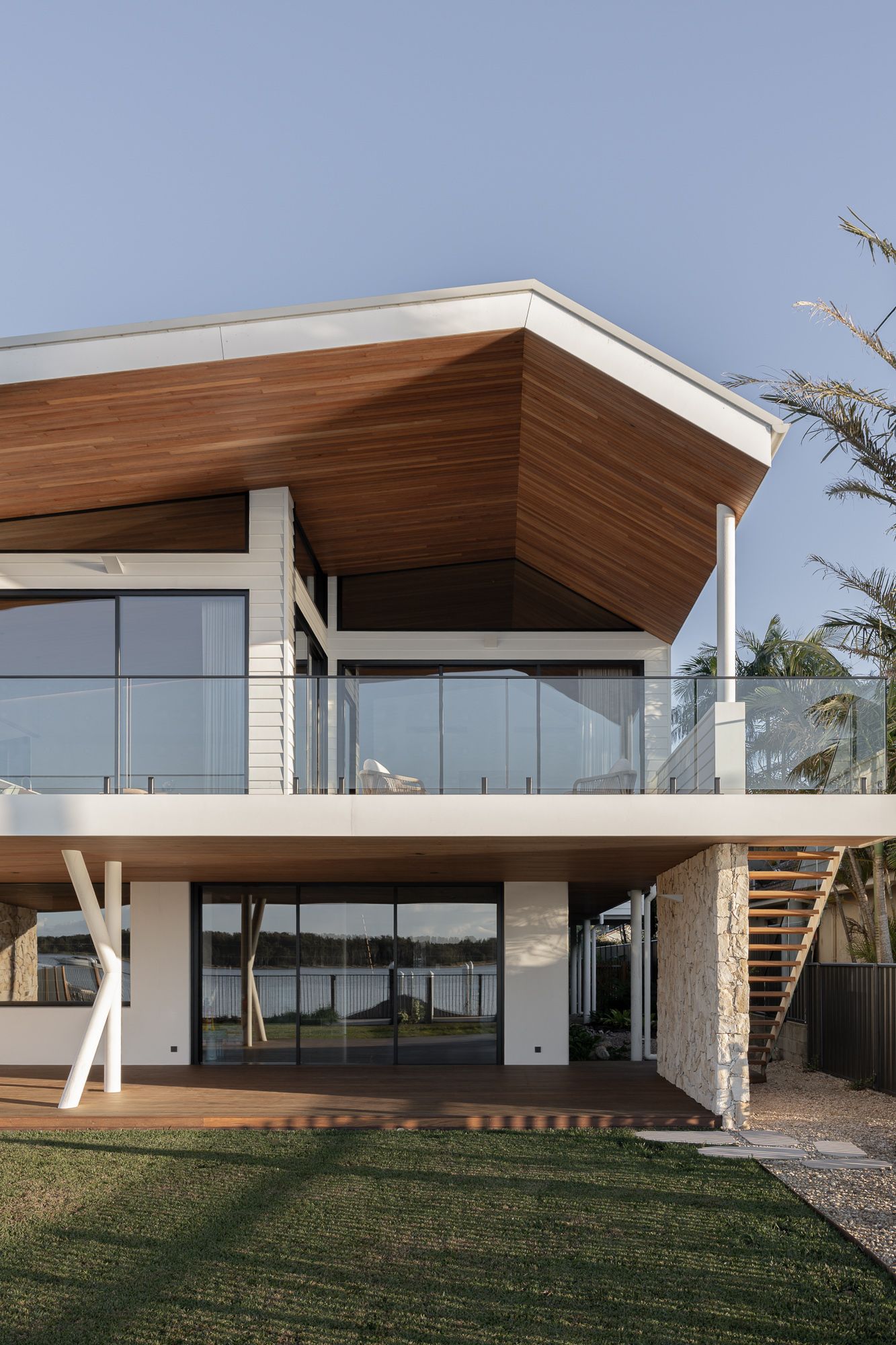 Rear elevation of a new coastal home in Shoalhaven with a timber-lined raked roof, glass balcony and open lawn.