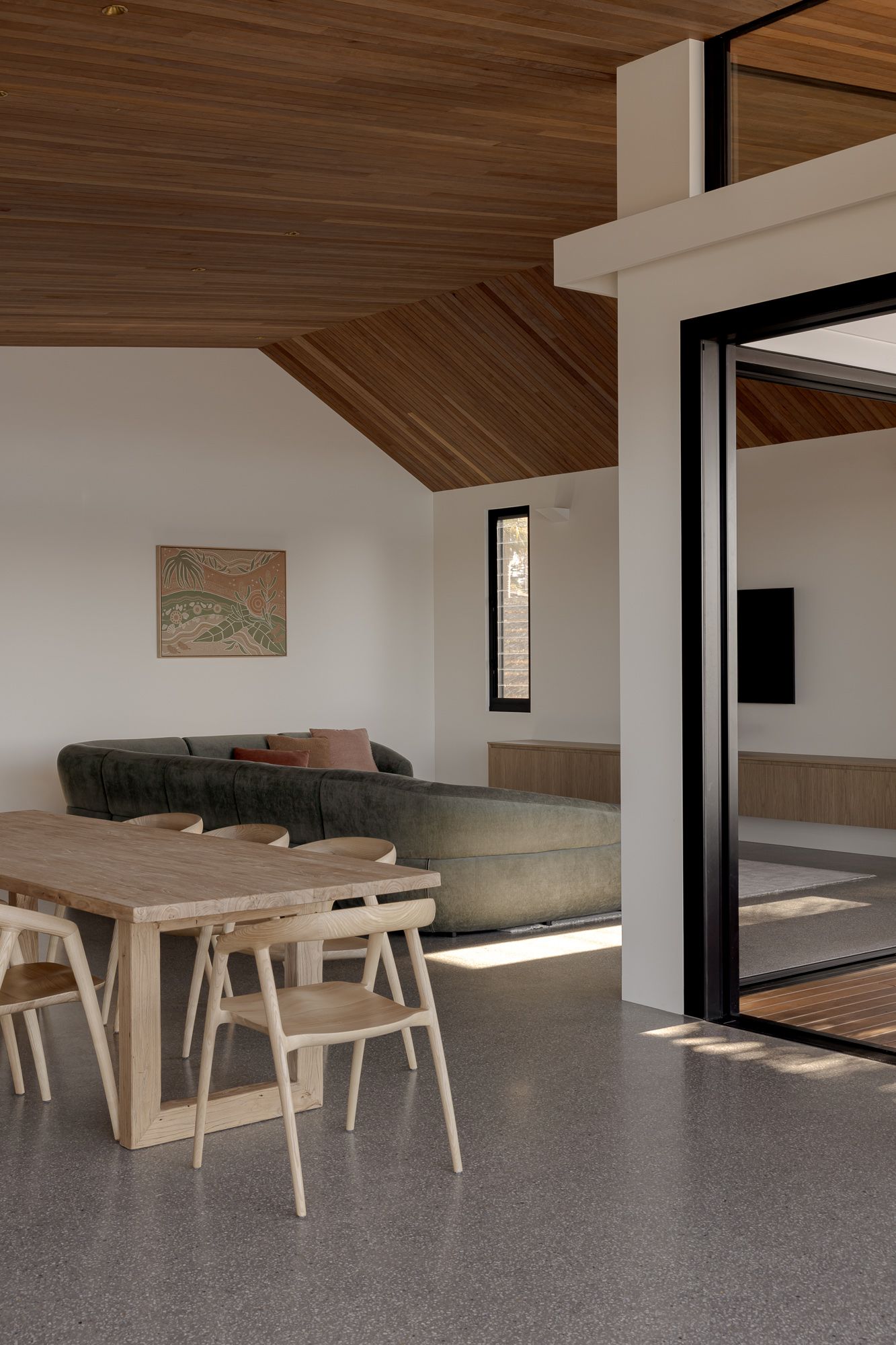Dining and living space with a timber-lined ceiling and floor-to-ceiling glass doors in a new riverside home in Shoalhaven.