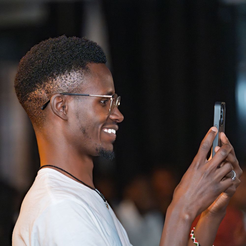 Smiling young man with glasses taking a photo on his smartphone at an indoor event.