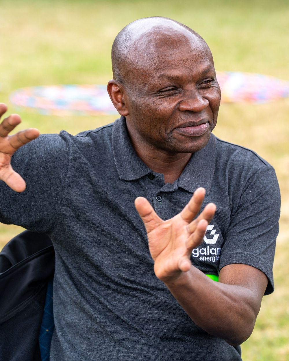 Older man in Galana Energies polo shirt gestures expressively outdoors.
