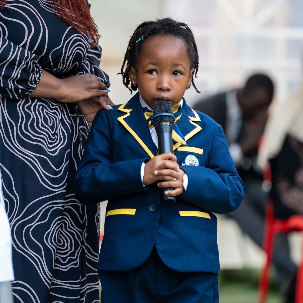 Young child in navy blue blazer holds microphone confidently at formal school event.