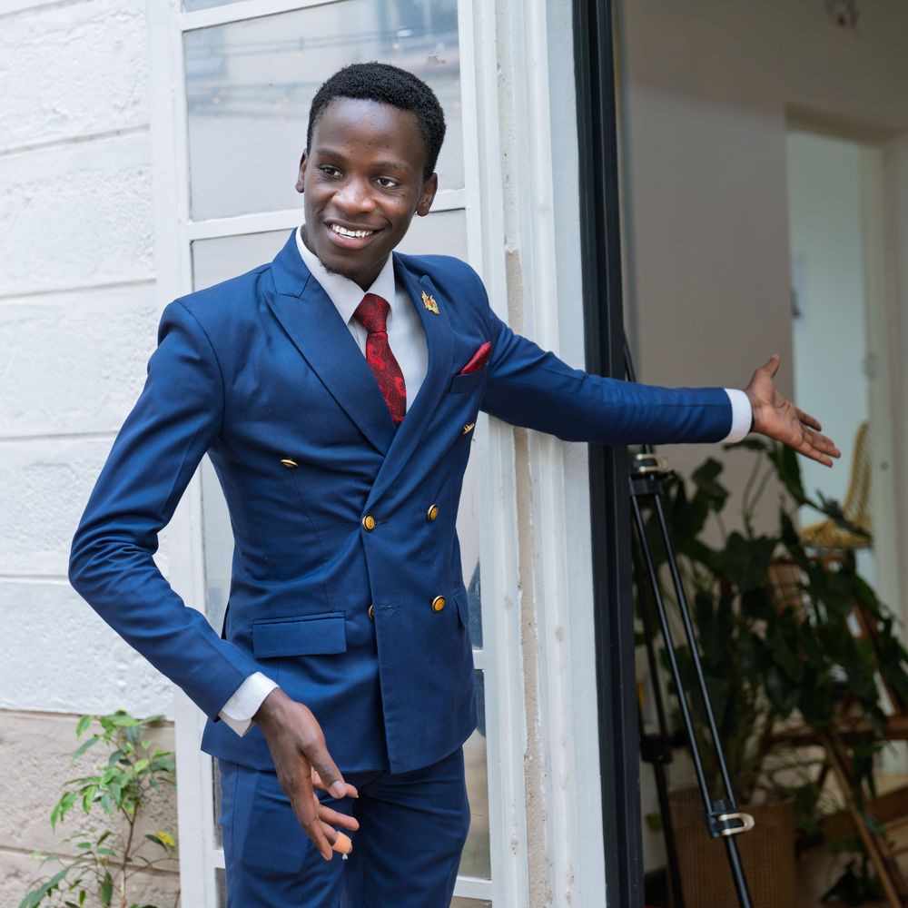 Stylish young man in navy blue double-breasted suit with red tie posing at a doorway.
