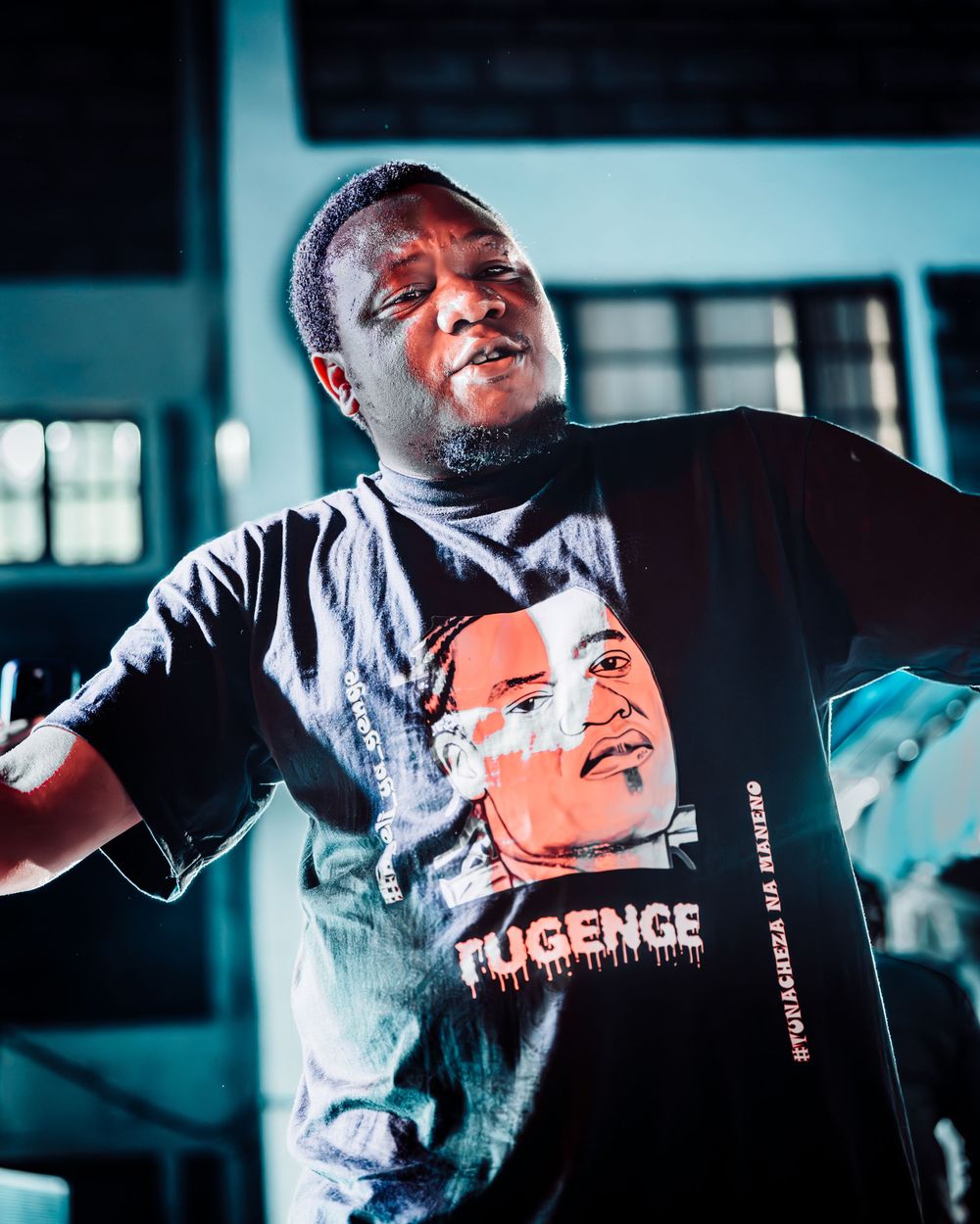 Energetic performer in black graphic t-shirt dancing under blue stage lights at live event.