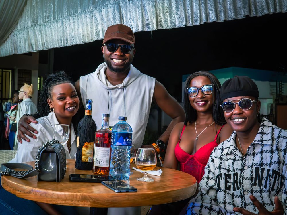 Group of four friends posing together at a bar table with bottles of liquor at a nightlife event.