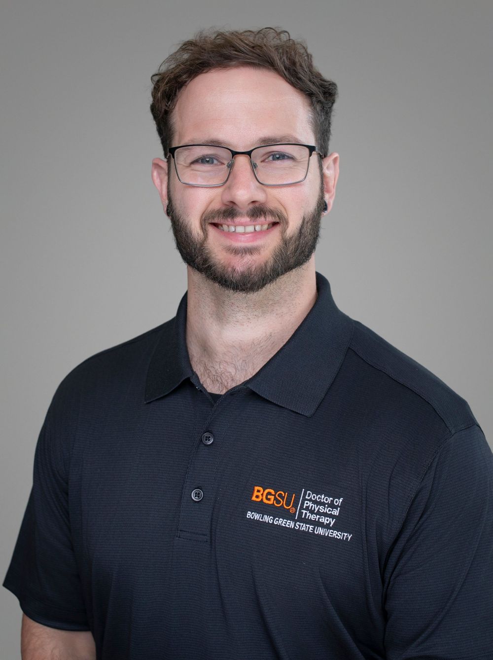 BGSU Doctor of Physical Therapy student smiling in navy polo shirt against gray background.