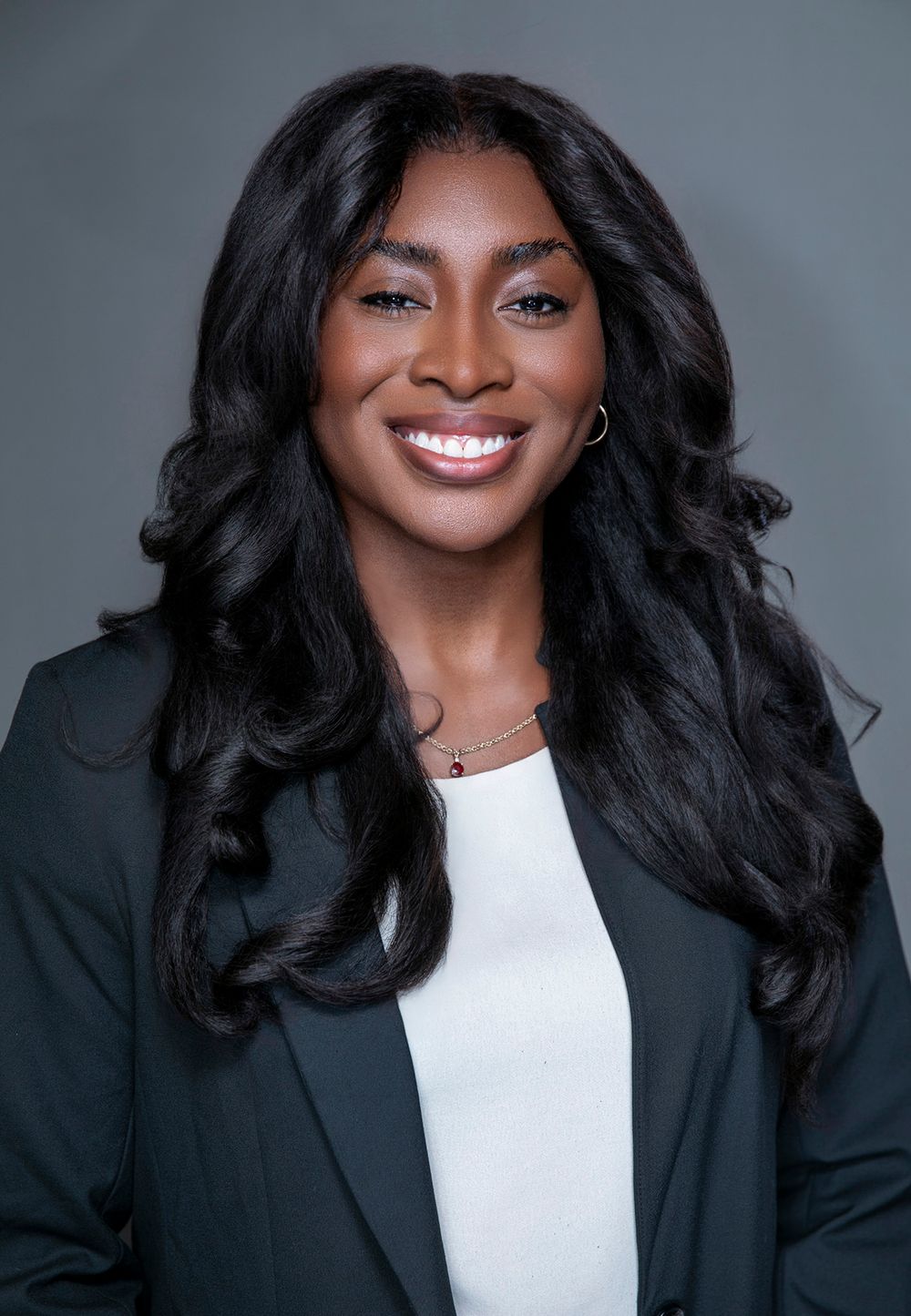 Professional headshot of a smiling woman with long black hair wearing a dark blazer and white top.