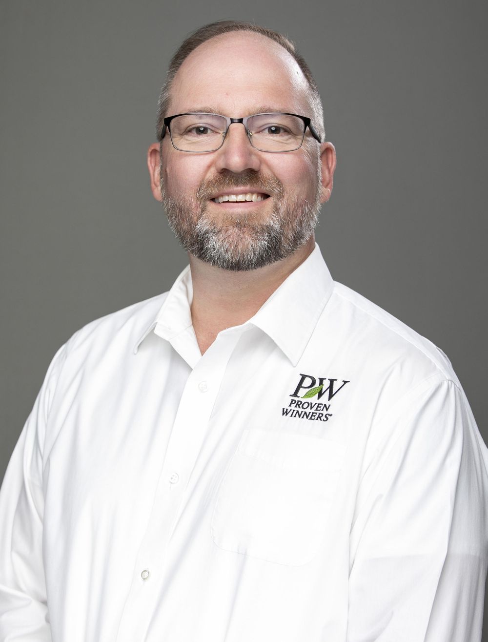 Professional headshot of a smiling man with glasses and beard wearing a white Proven Winners branded shirt.