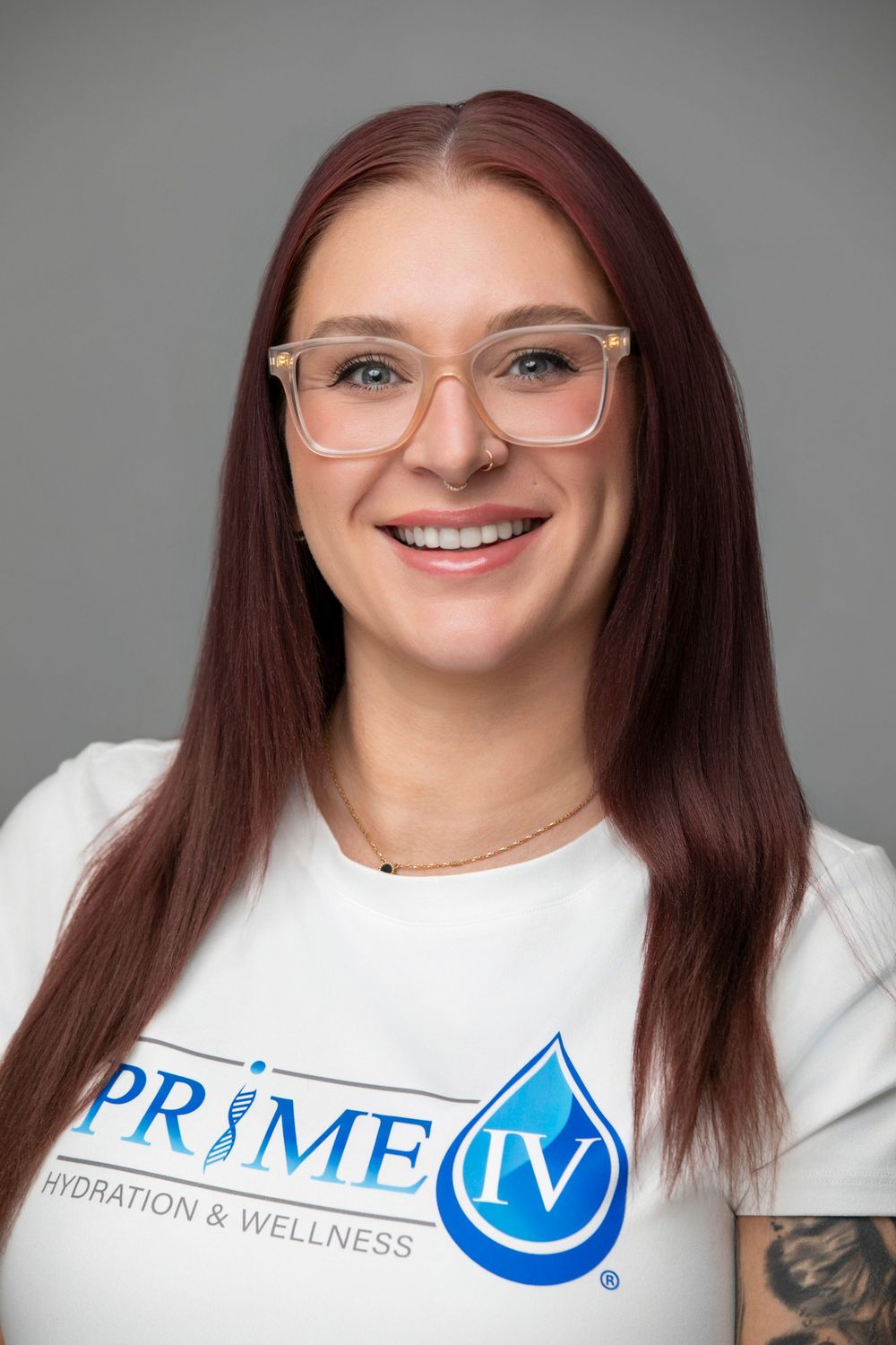 Smiling woman with red hair and glasses wearing a Prime IV Hydration & Wellness white t-shirt.