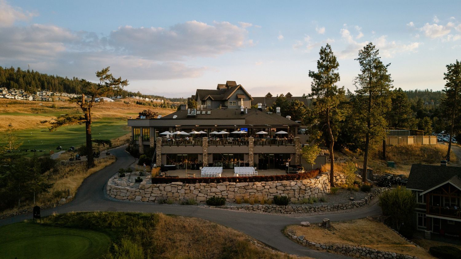 predator ridge wedding venue in vernon bc on golf course with string lights, guests seated, couple at altar, surrounded by trees and hills.