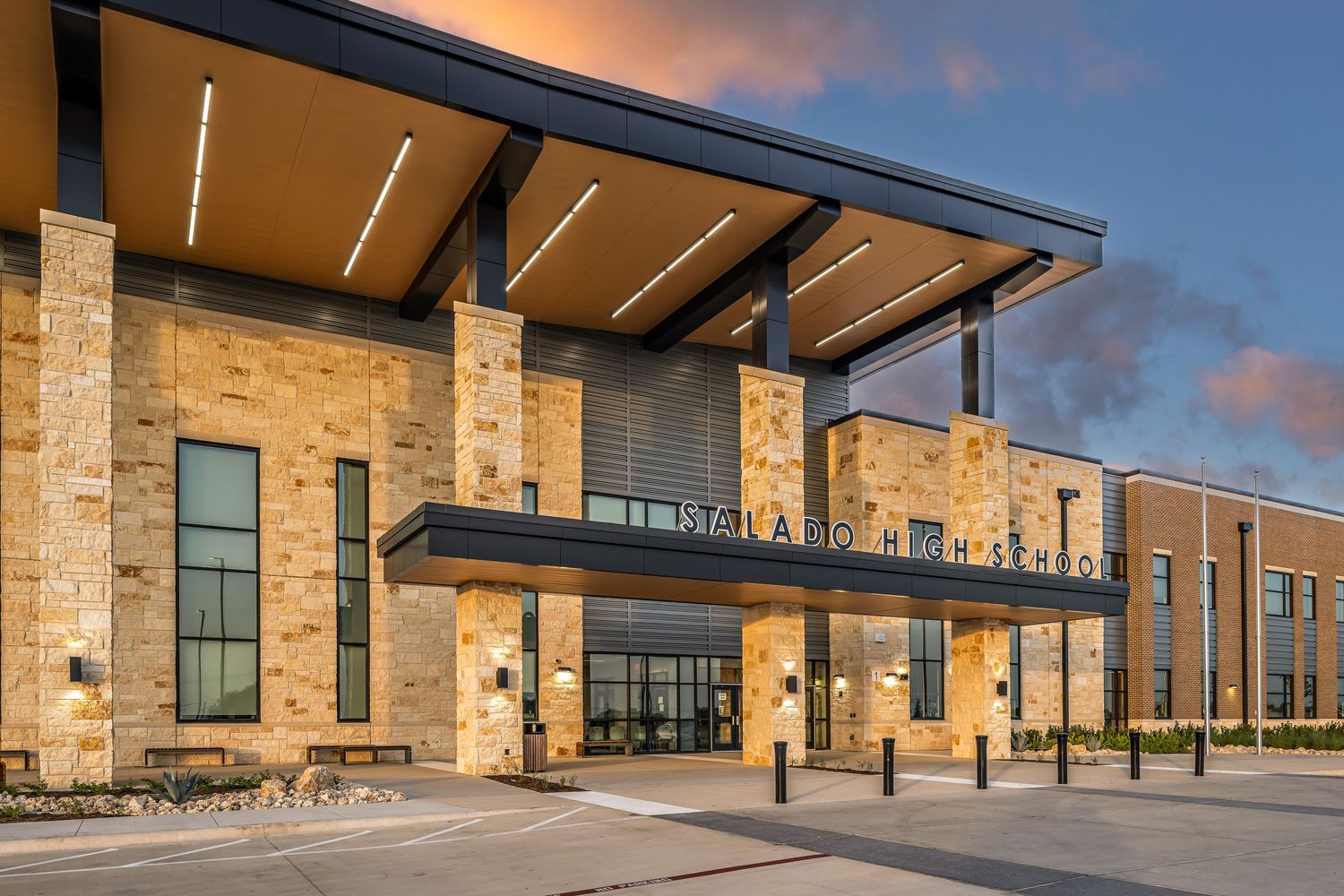 Modern stone and glass school building exterior illuminated at dusk with sleek architectural lighting and covered entrance.