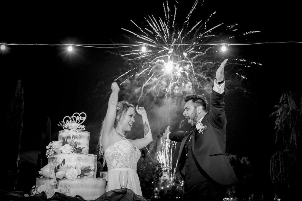 Black and white photo of bride and groom cutting wedding cake with fireworks celebration.