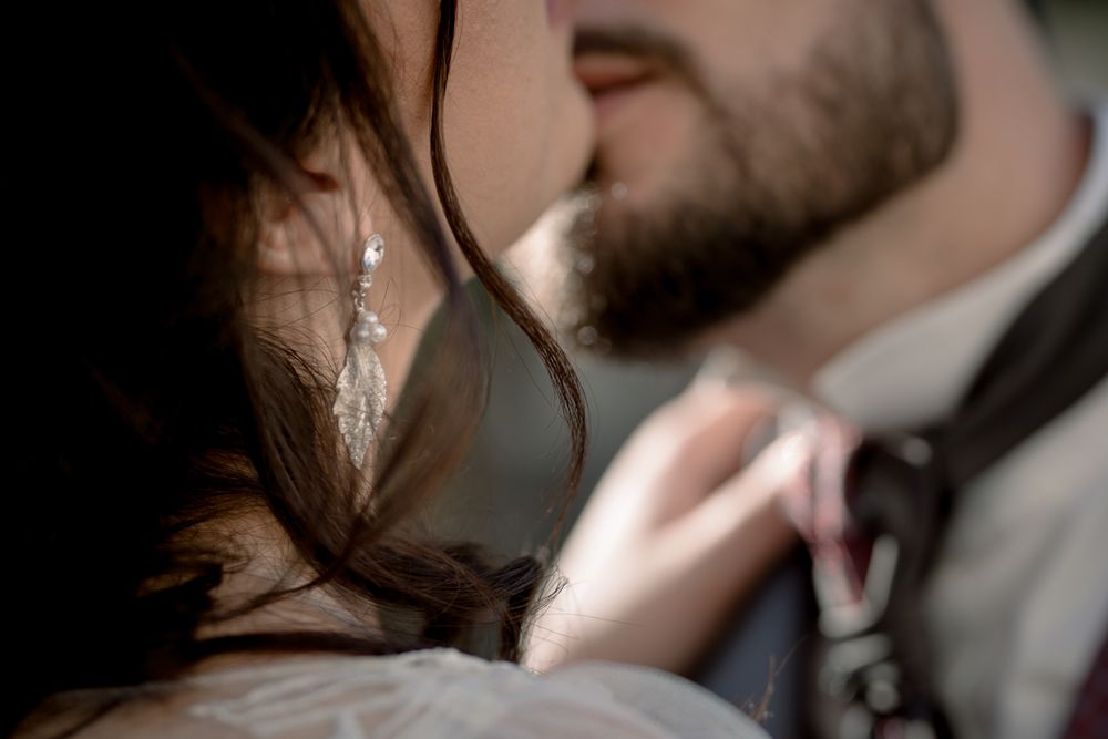 Romantic close-up of bride and groom almost kissing, bride wearing crystal earring and white dress.
