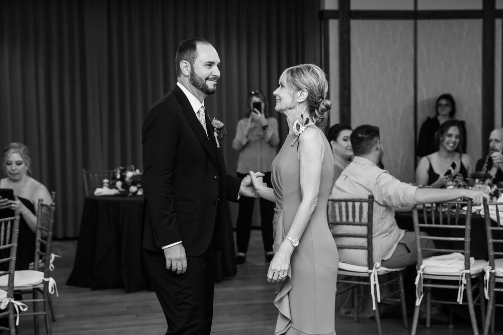 Black and white photo of groom and mother sharing a dance at elegant wedding reception.