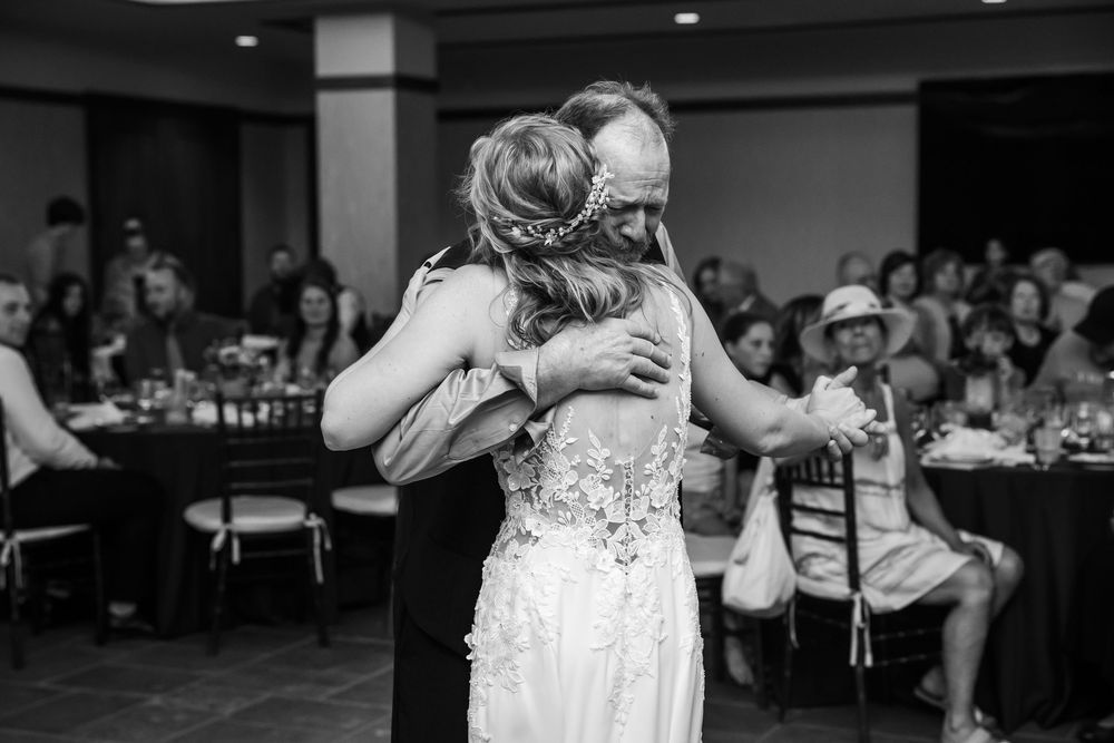 Black and white photo of bride and father sharing emotional first dance hug at wedding reception.