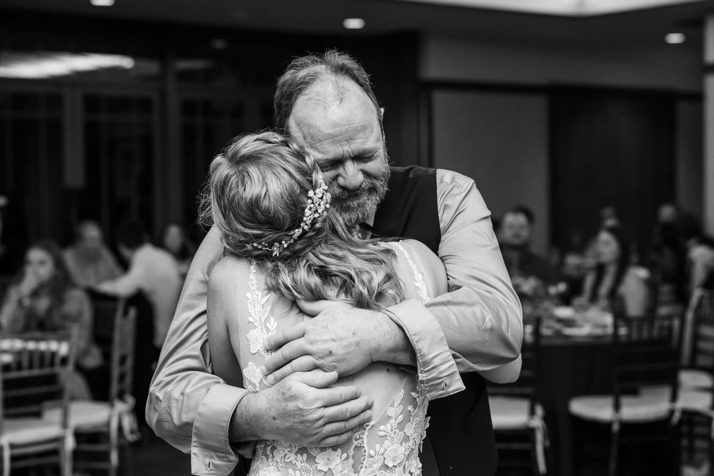 Father and bride share emotional hug during wedding reception father-daughter dance in elegant ballroom.