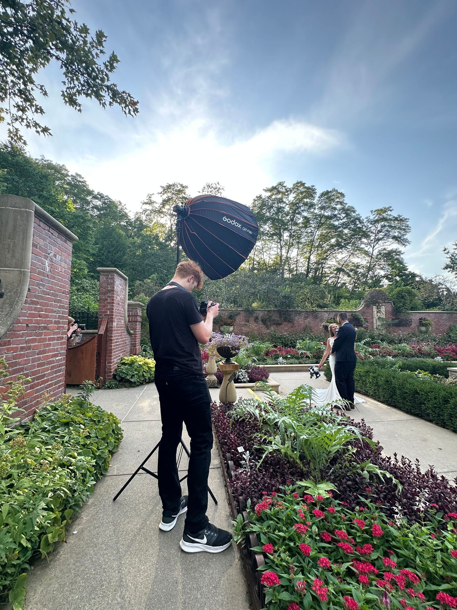 Photographer with large camera lens assisted by two people at an outdoor event on a sunny day.