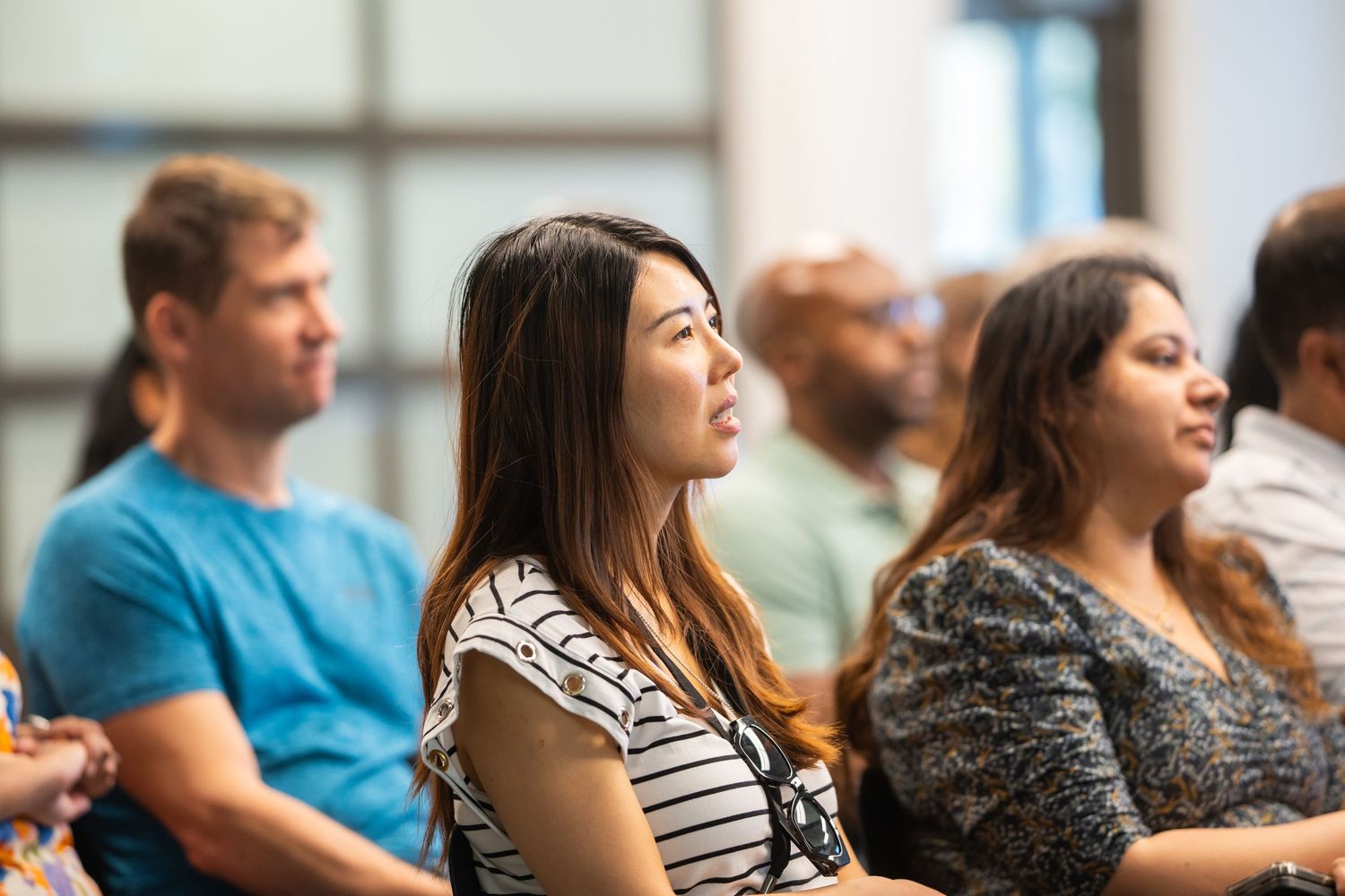 Diverse group of adults attentively listening during a seminar or conference session in a bright modern room.