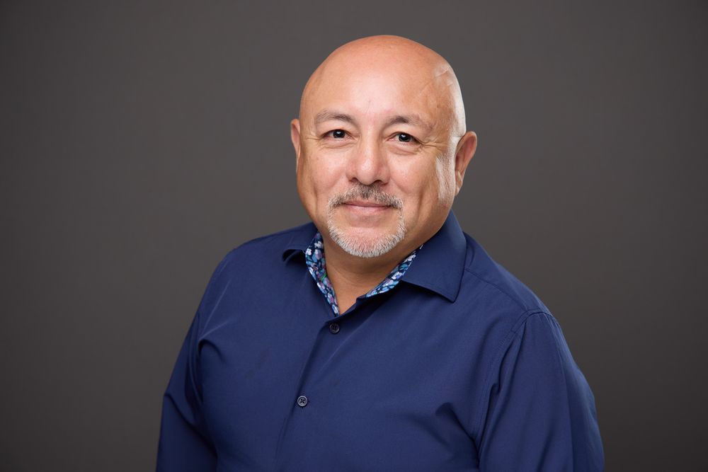 Professional headshot portrait of a person in a blue polo shirt against a dark background.