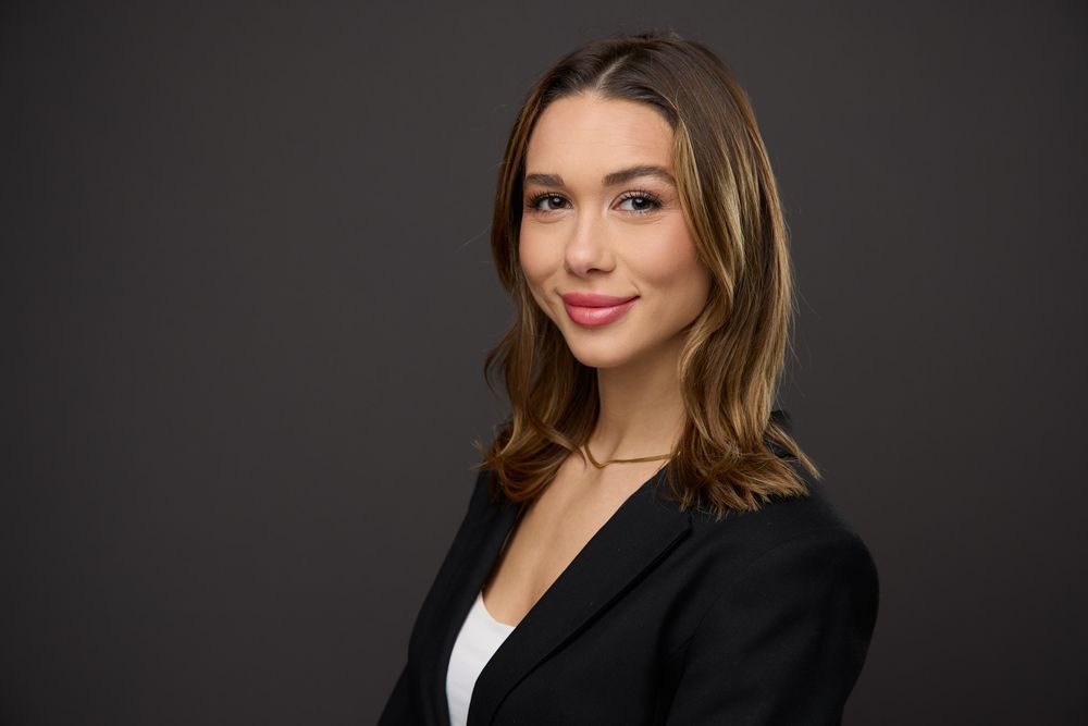 Professional headshot portrait of a woman wearing a black blazer and white top against a dark background.