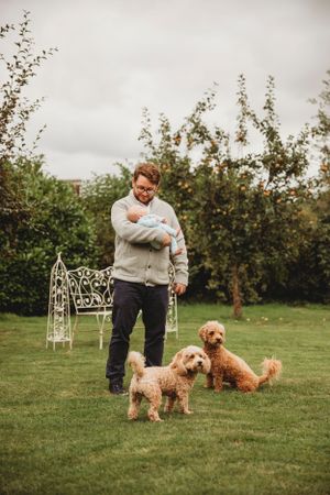 Person in gray sweater stands with two fluffy goldendoodle dogs on a lawn with ornamental garden furniture.