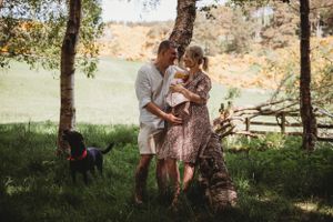 Family enjoys outdoor time with their dog under trees in a sunny countryside setting.